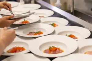 Prato de catering corporativo com apresentação de alimentos sofisticados e bem montados em pratos brancos, sendo preparado para evento corporativo.