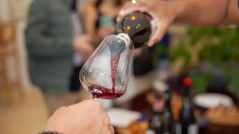 Degustação de vinho no winebar cellarcave, com foco na taça sendo preenchida e clima aconchegante ao fundo.